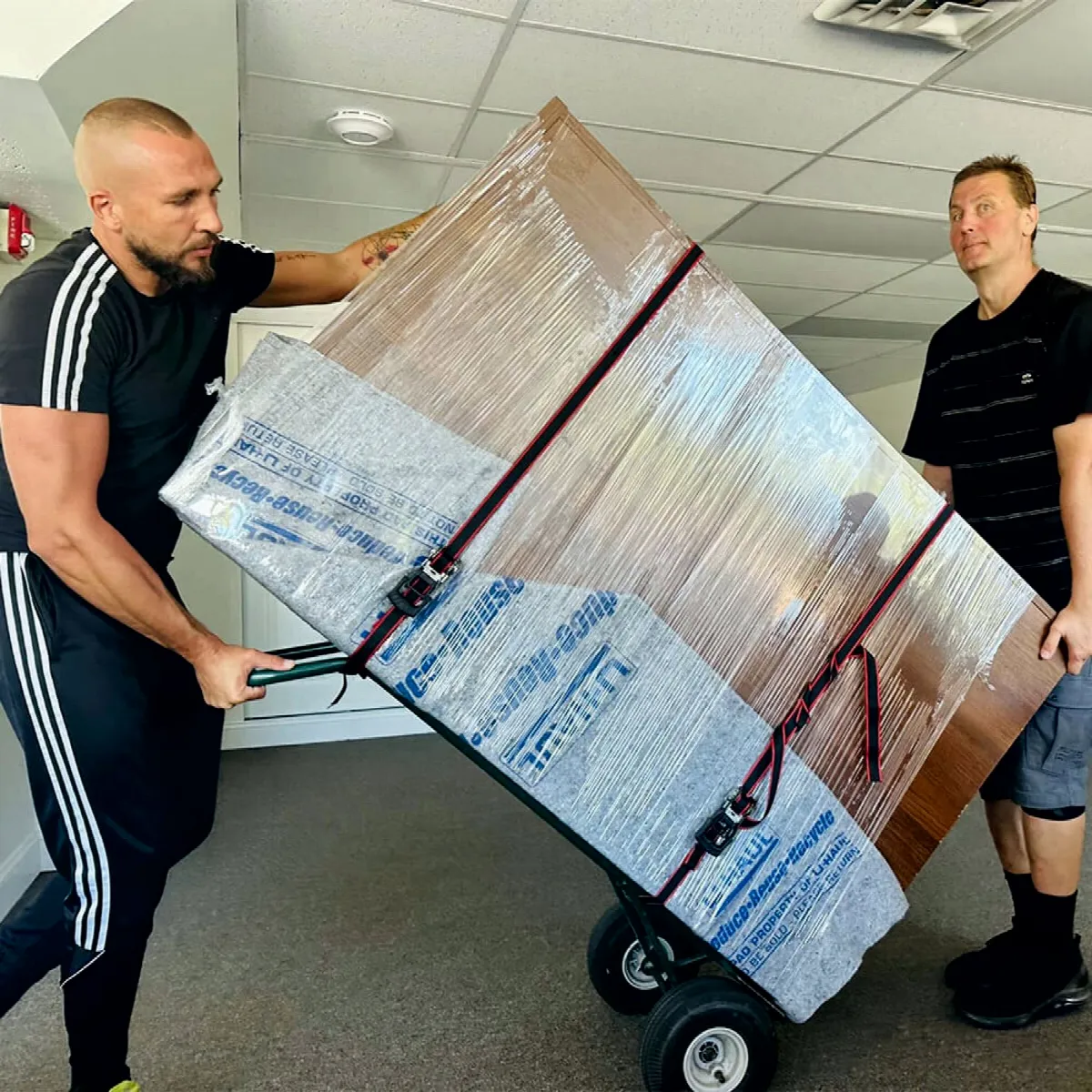 CarePhilly Movers wheeling a wrapped wardrobe on a dolly
