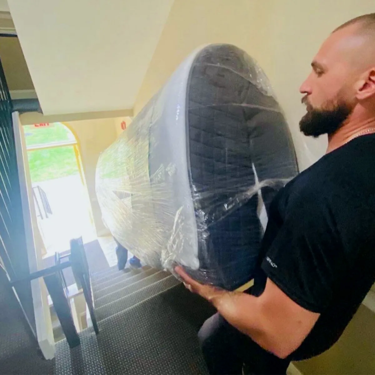 A mover carrying a wrapped armchair down a stairwell