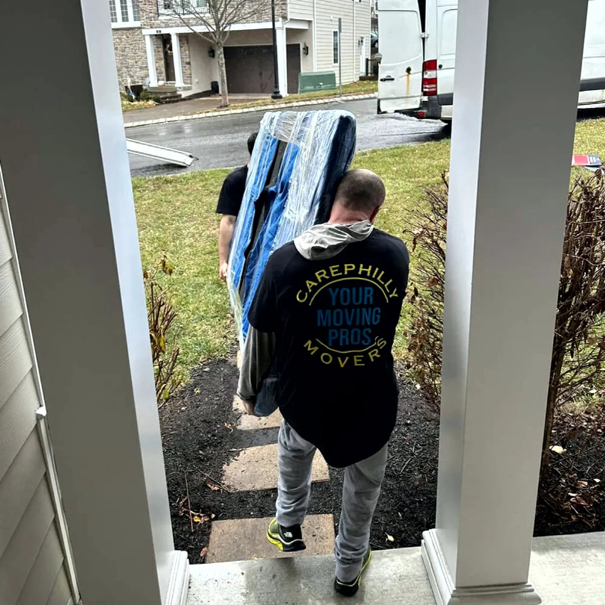 A mover in a CarePhilly shirt carrying a wrapped mattress out of a house