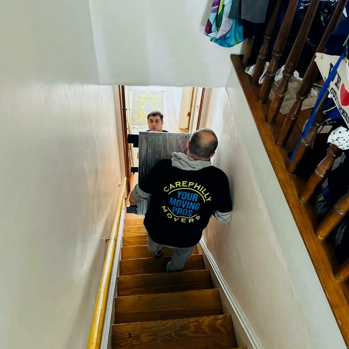 Two movers carrying furniture up a narrow staircase inside a home