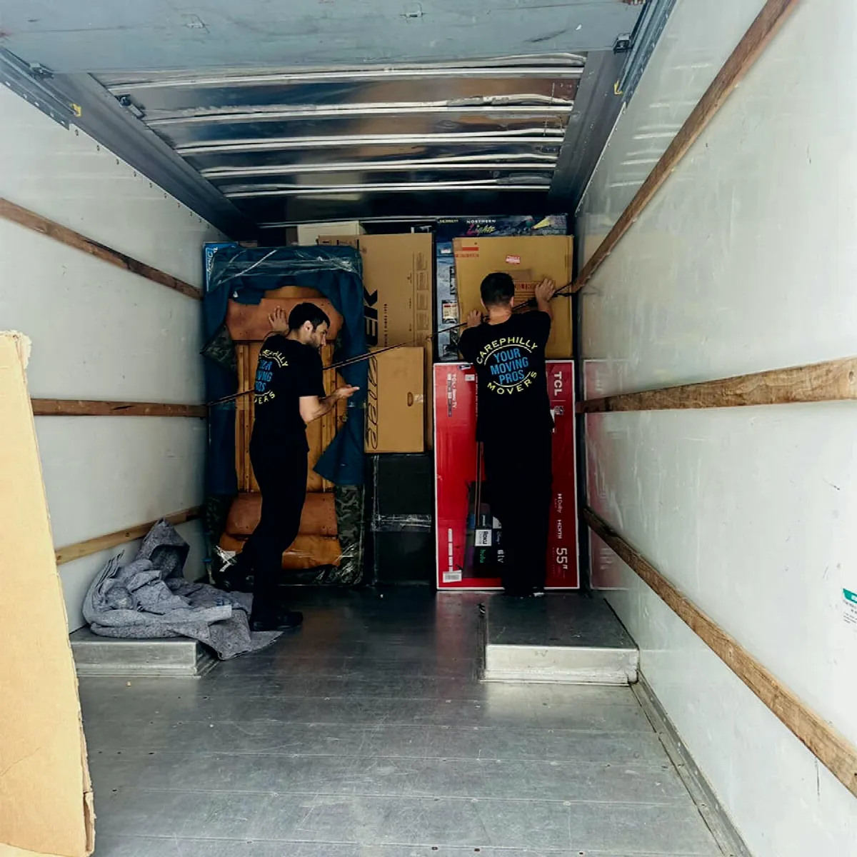 Two movers securing boxes and a television against the truck wall