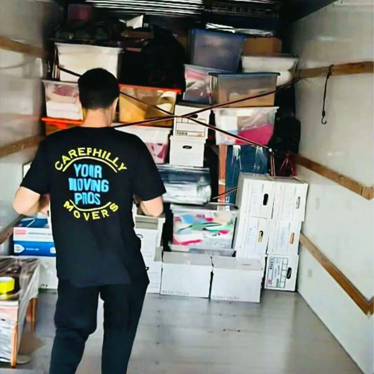 A mover loading archive boxes, held by straps across the truck